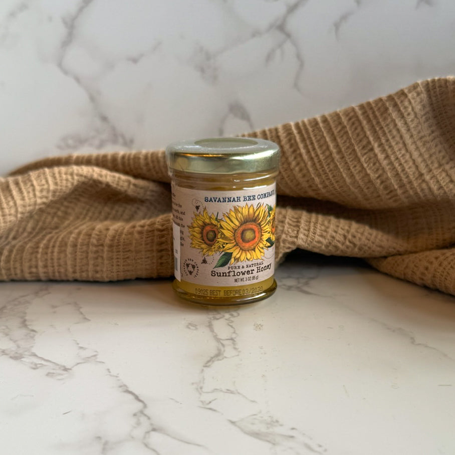 Jar of Savannah Bee Company sunflower honey on a marble surface with burlap fabric.